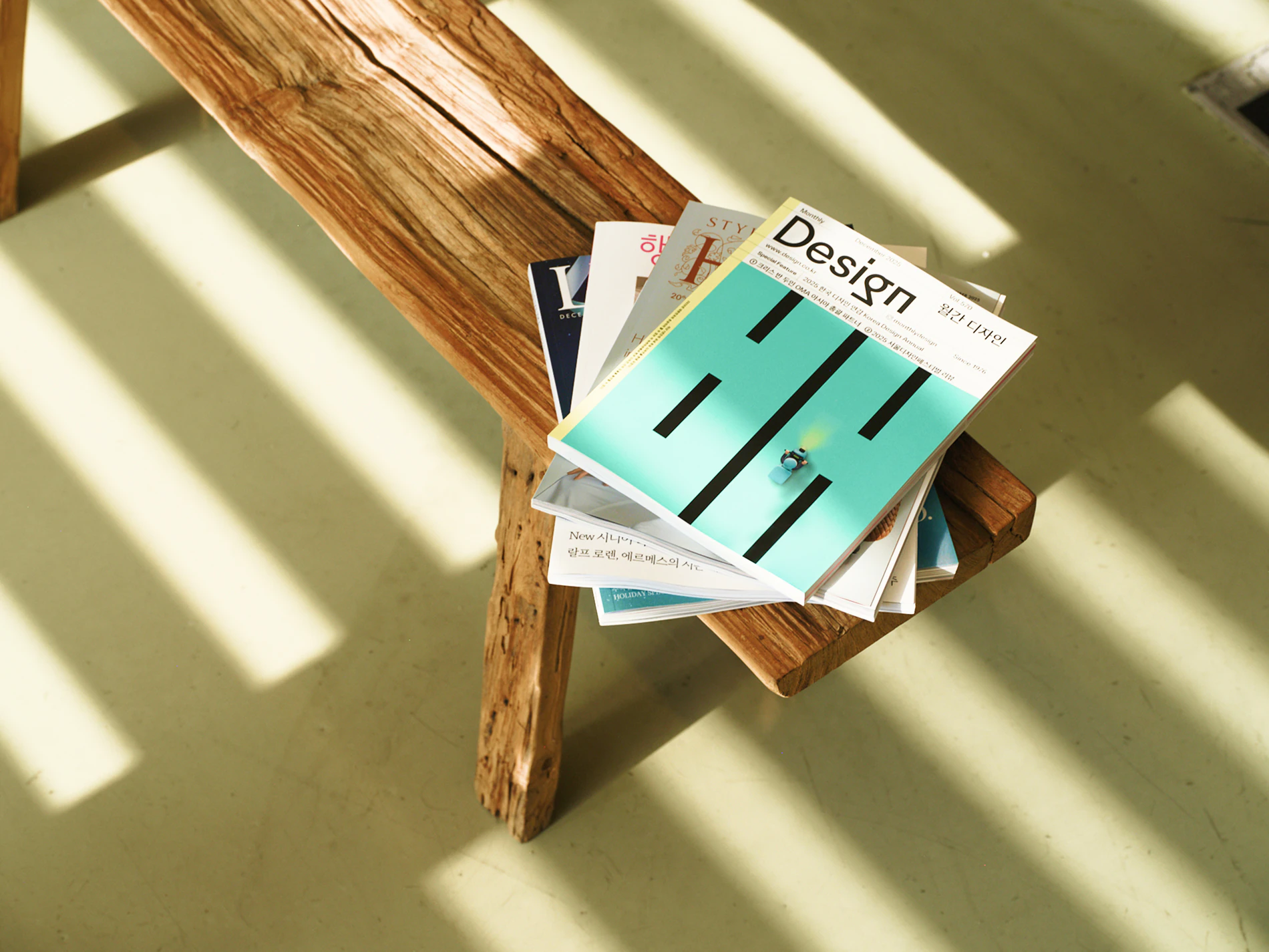 A stack of design house magazines on a wooden bench in sunlight